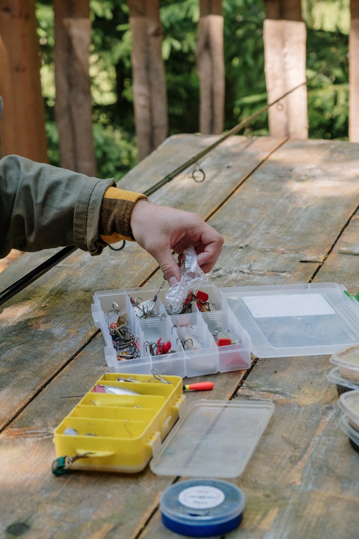 A hand organizing fishing equipment on a rustic outdoor table, ideal for anglers.